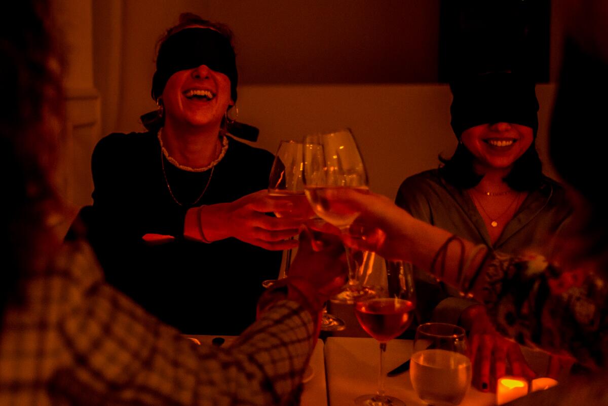 Blindfolded diners toast each other in a candlelit restaurant for Dining in the Dark, which will launch in May in San Diego.