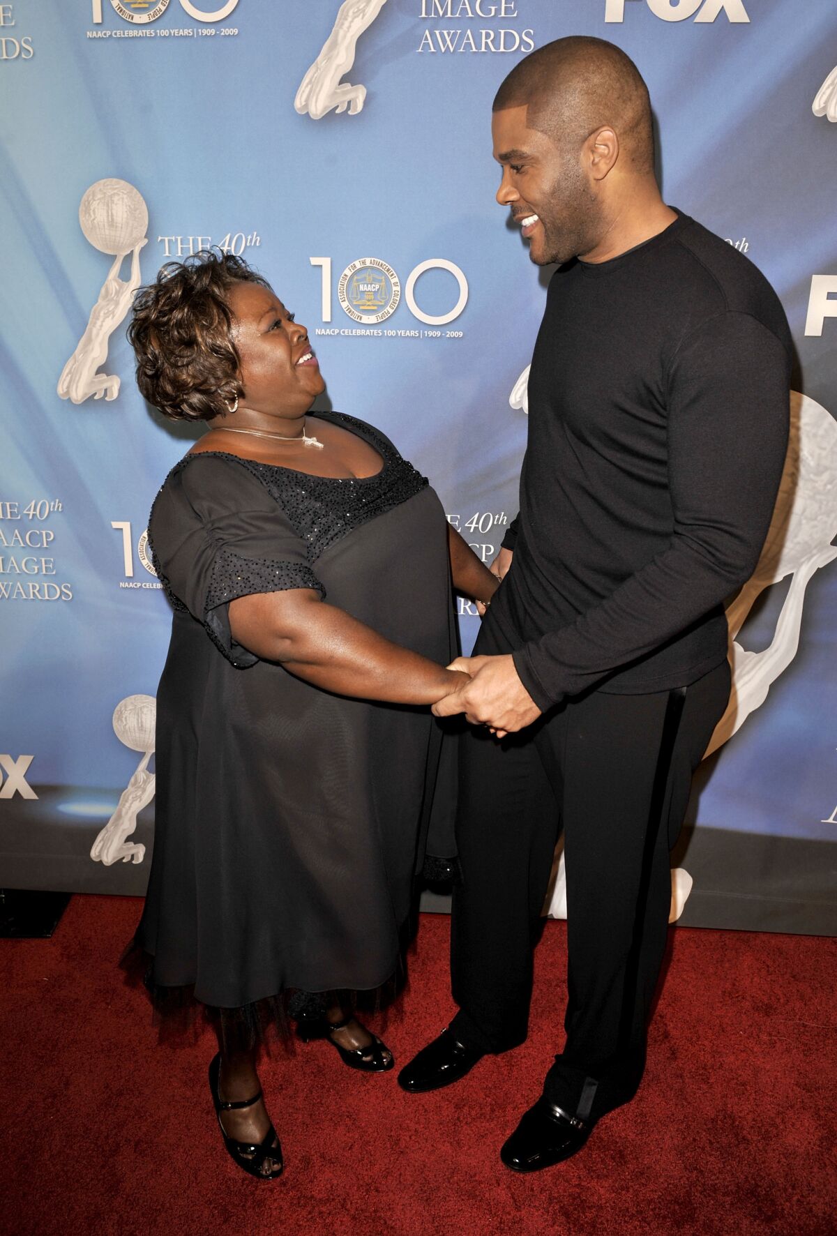 A woman and a man in evening attire hold hands and smile at each other