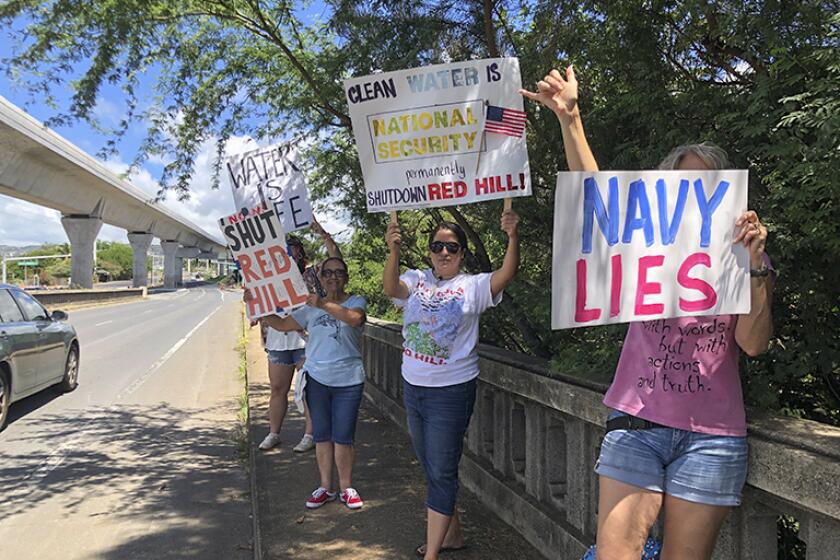FILE - Protestors upset with the Department of Defense's response to the leak of jet fuel into the water supply hold signs outside the gate at Joint Base Pearl Harbor-Hickam, Hawaii, Friday, Sept. 30, 2022. Three active-duty military members are taking the first step toward suing the U.S. government over jet fuel that contaminated drinking water in Hawaii. Their attorneys say the pre-litigation claim forms will allow them to later file a federal lawsuit in Honolulu. In 2021, jet fuel spilled from a drain line at a storage facility that flowed into a drinking water well and into the Navy's water system. (AP Photo/Audrey McAvoy, File)