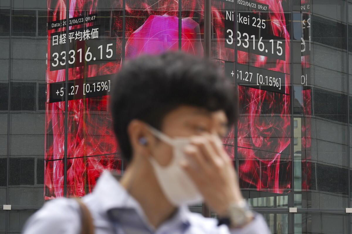 A person walks in front of an electronic stock board showing Japan's Nikkei 225 index