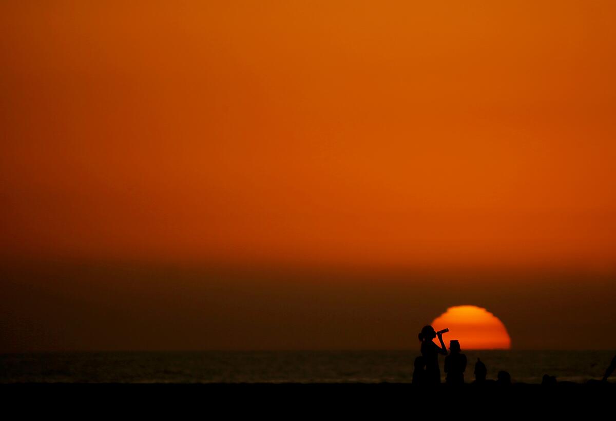 HUNTINGTON BEACH, CALIF. - DEC. 6, 2023. Beachgoers are framed against the setting sun at the end of a warm day in Huntington Beach. Scientists say that Novemeber was the sixth straight month to set a heat record. (Luis Sinco / Los Angeles Times)