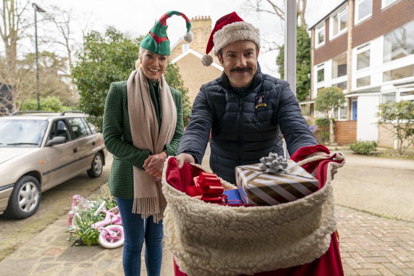 A woman dressed as an elf and a man dressed as Santa deliver presents.