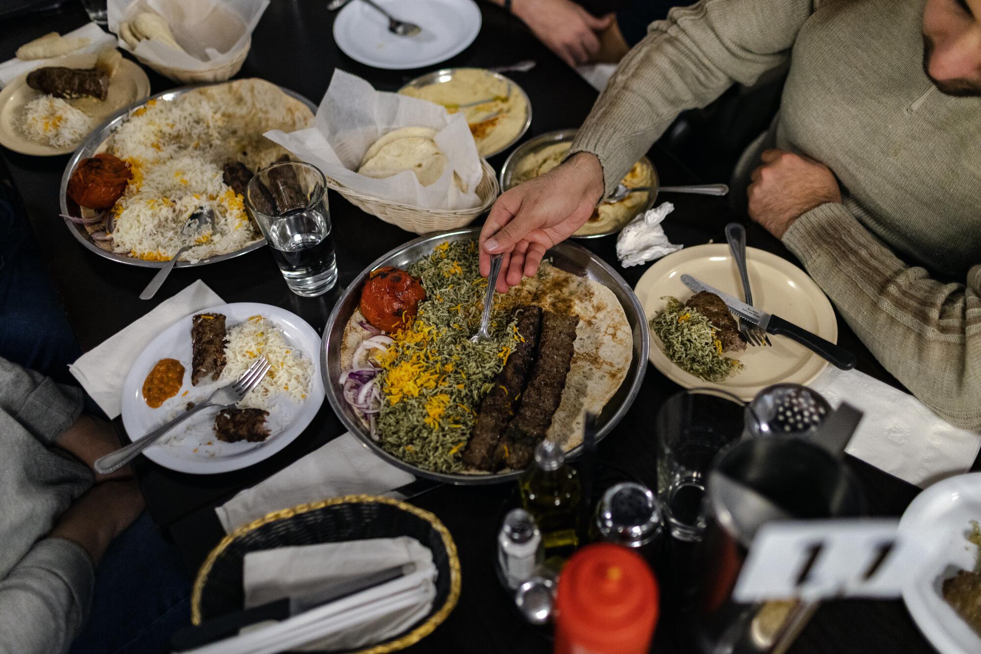 people reach for food at a shared meal at a Kabob restaurant