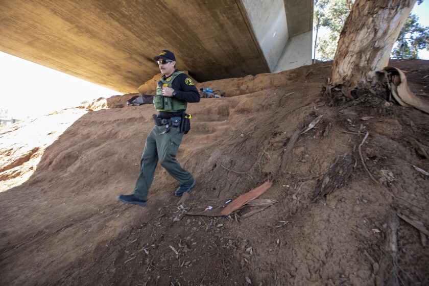 In this file photo from December, Sheriff's Deputy Aaron Bert heads back to his vehicle after speaking with homeless people under a bridge on Magnolia Street in El Cajon. Bert is one of two deputies assigned to the department's Homeless Assistance Resource Team, which will add four more deputies under a plan approved by the County Board of Supervisors on Tuesday.