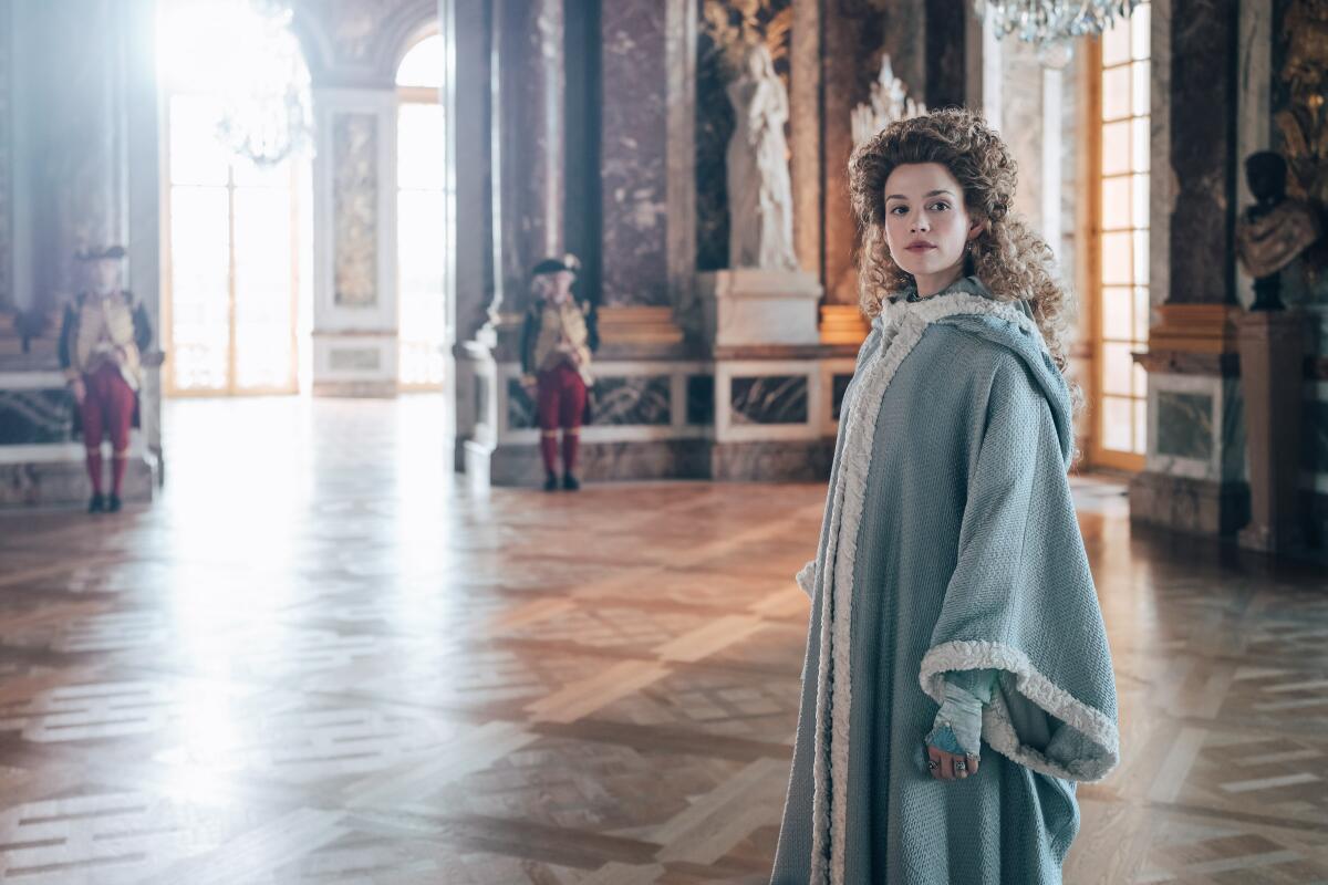 A woman with curly hair in a light blue robe stands in an large open room.