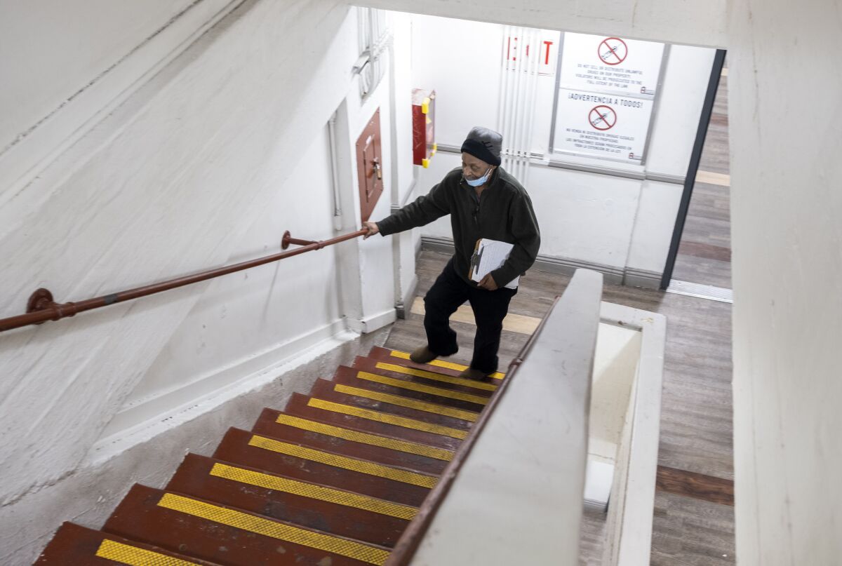 An elderly man holds on to the railing of a staircase near the bottom as he walks up the stairs.