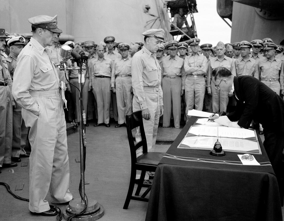 U.S. Gen. Douglas MacArthur, left, watches as Japanese Foreign Minister Mamoru Shigemitsu signs surrender document.