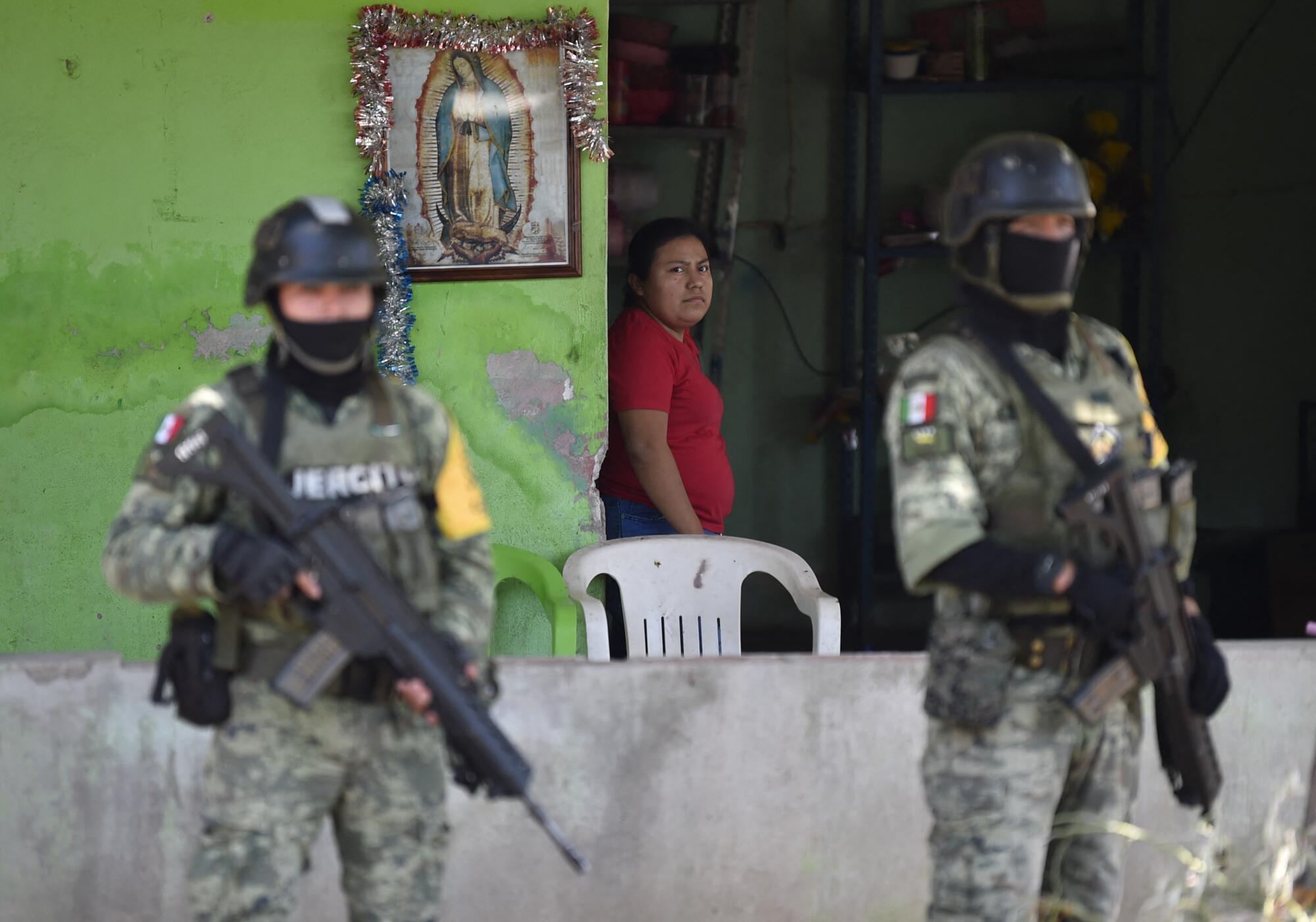 A woman watches from her home as soldiers patrol