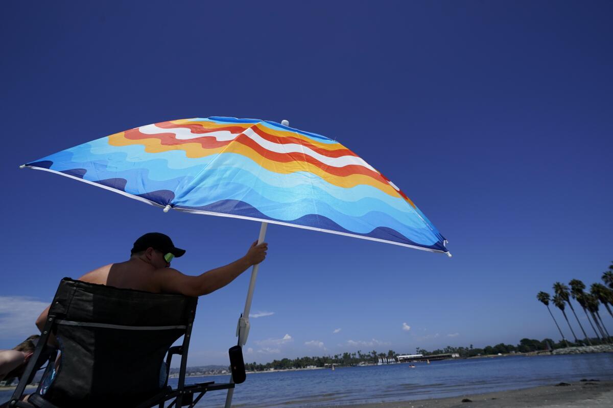 Seth Salmond, of Alpine, Calif., cools off under an umbrella along Mission Bay, Friday, Sept. 2, 2022, in San Diego. Salmond and his family came west for the day to get away from the heat farther east in San Diego County. Californians sweltering in the West's lengthening heat wave have been asked to reduce air conditioning and cut other electricity use again to prevent stress on the state's electrical grid that could lead to rolling blackouts. (AP Photo/Gregory Bull)