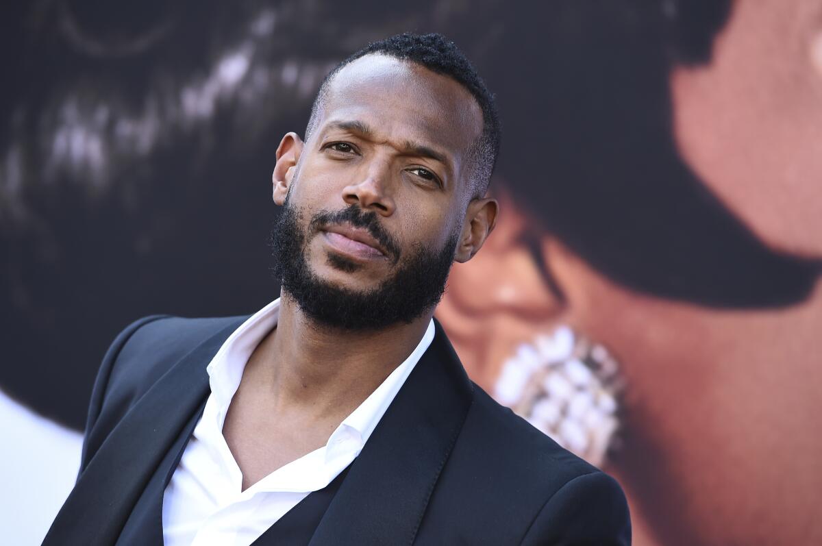 Marlon Wayans looks up with a slightly furrowed brow while wearing a dark jacket and open-collar white shirt