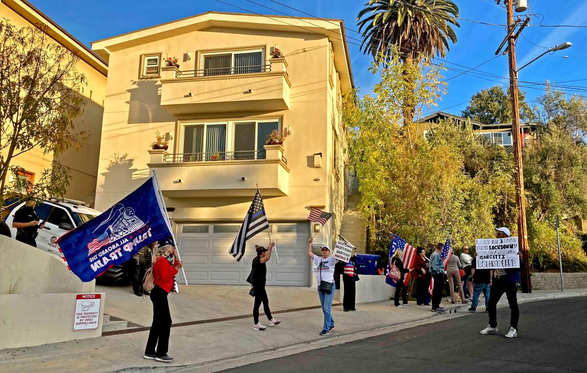 Protesters wave signs and flags in front of a home.