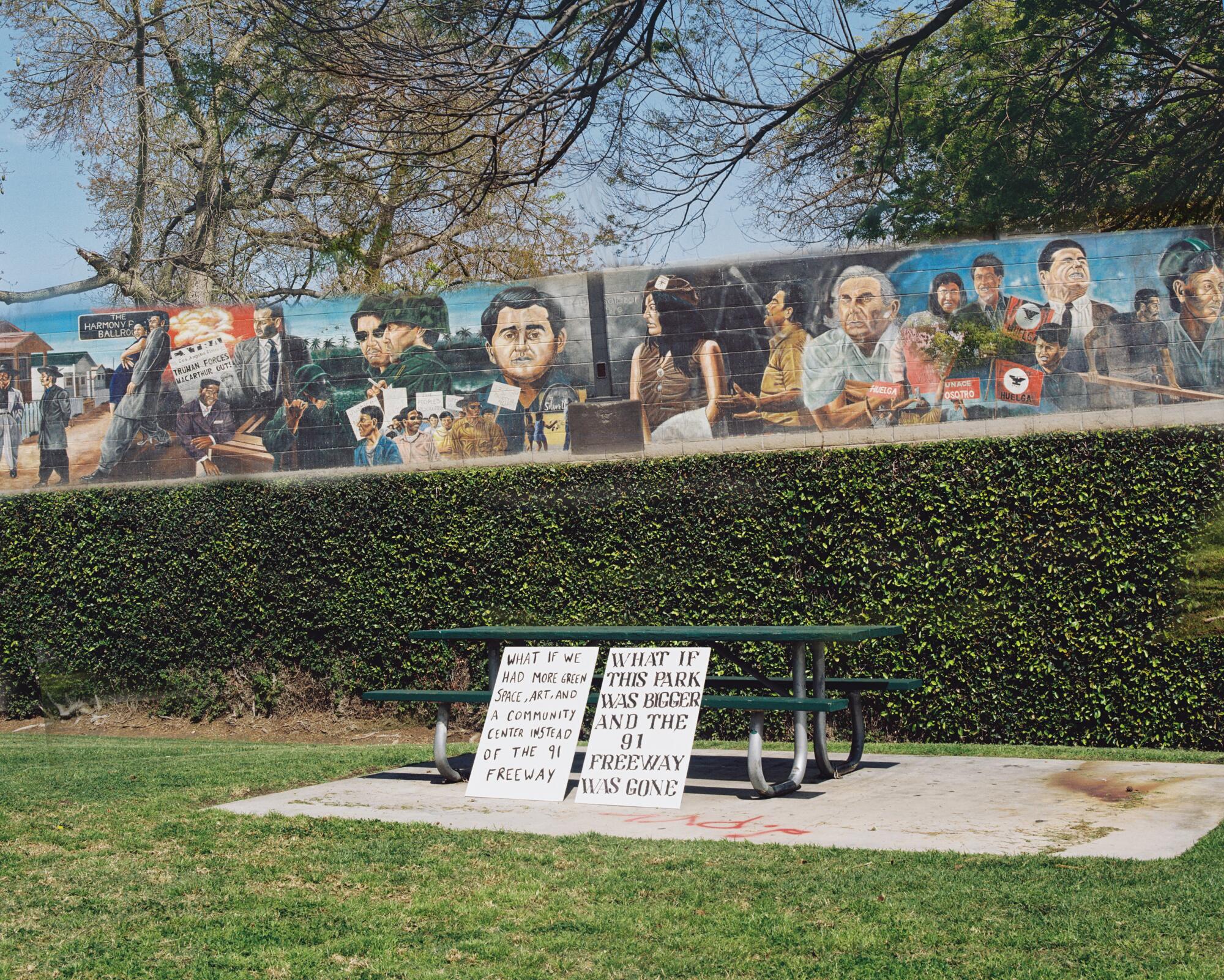 The same signs lean against a park bench, a mural overtaking the freeway wall on the other side. 