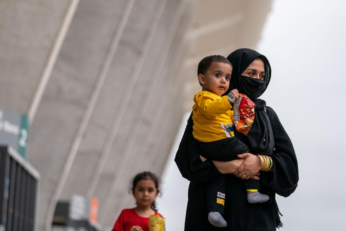 A woman carries a young child who is holding a bag of snacks  