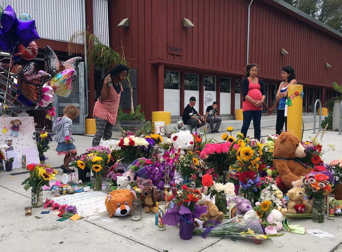 People gather around a makeshift memorial of flowers, toys and balloons