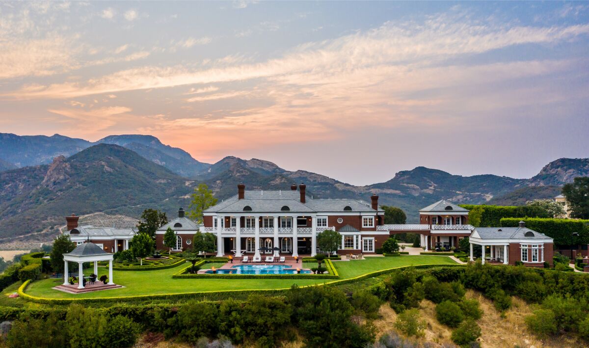 A red-brick Colonial-style estate with a massive green lawn and pool on a hilltop at sunset