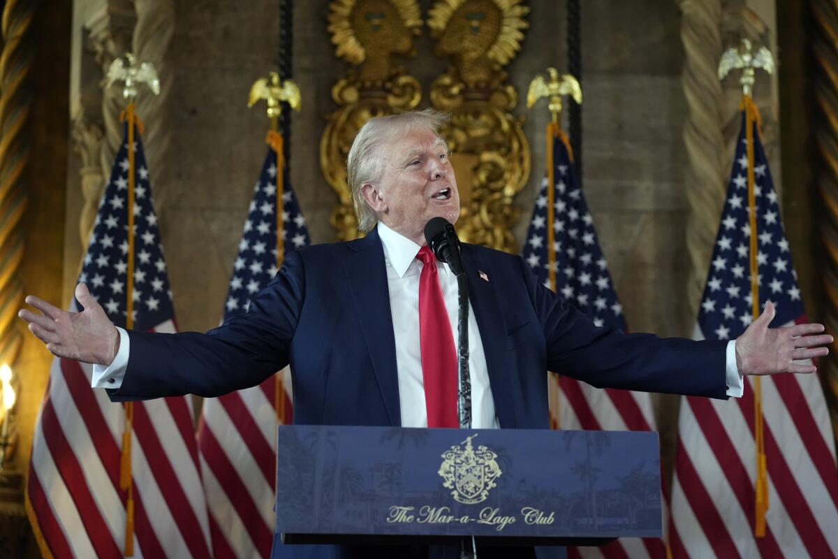 Donald Trump gesturing and speaking in front of a row of American flags during a news conference.