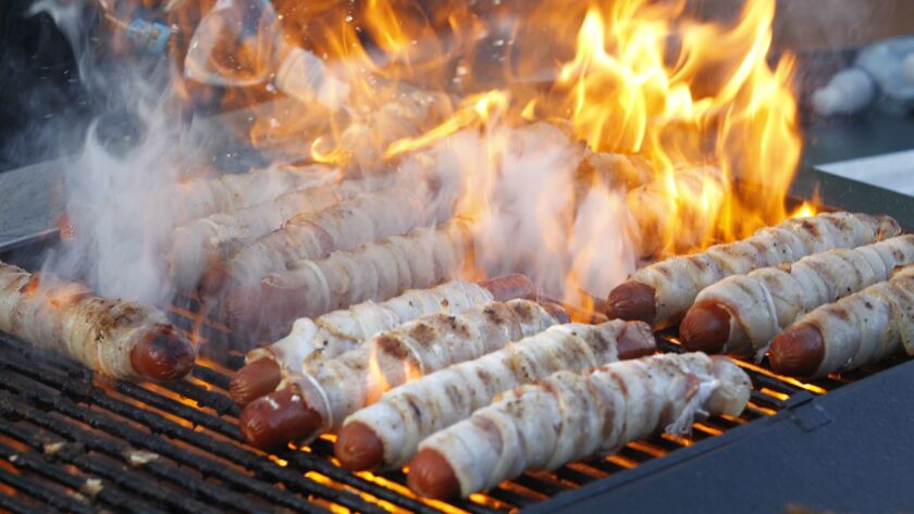 Bacon-wrapped hot dogs cook on the grill.