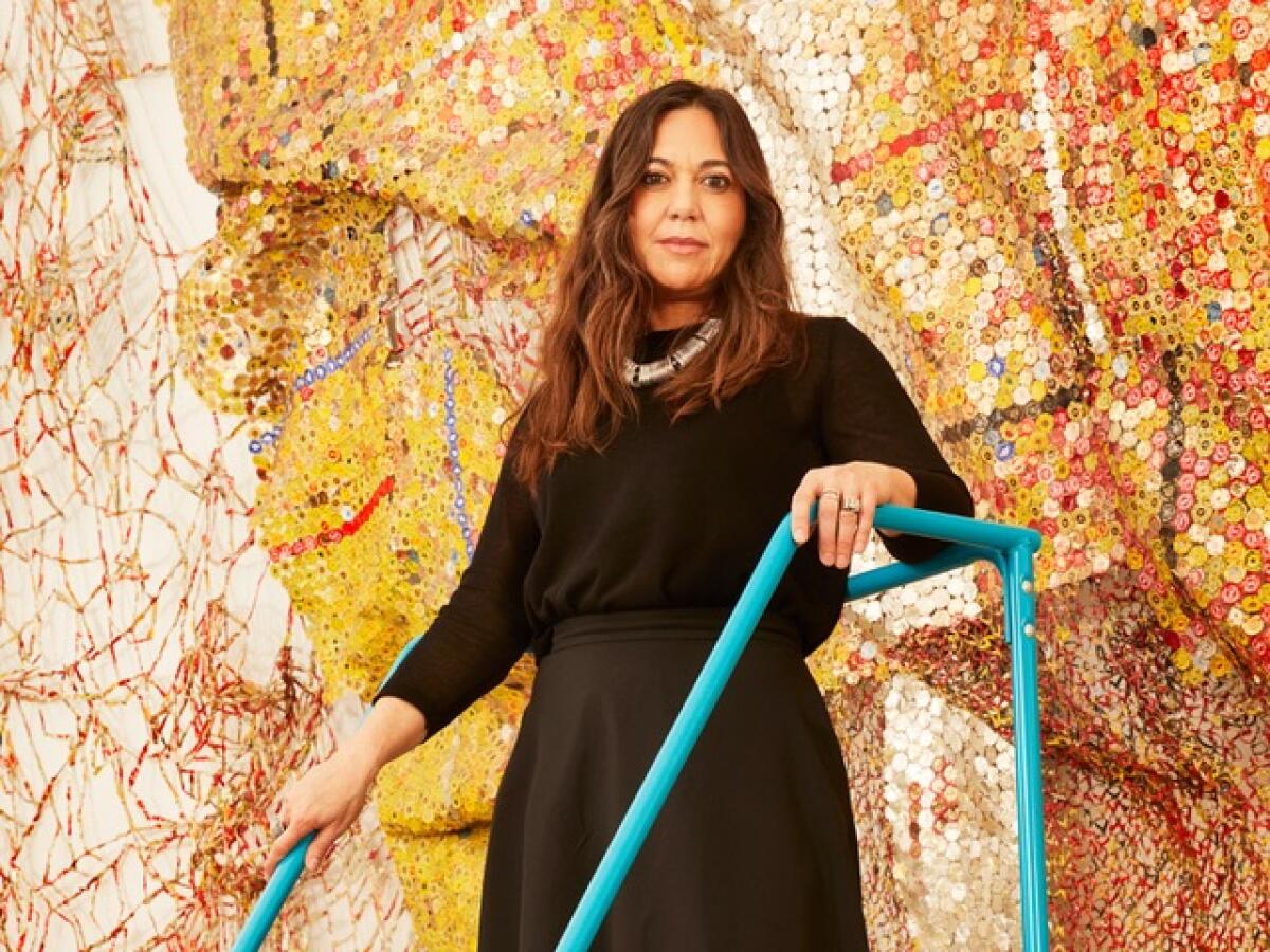 A woman stands on a ladder before a glittering wall sculpture made from crushed bottle caps.