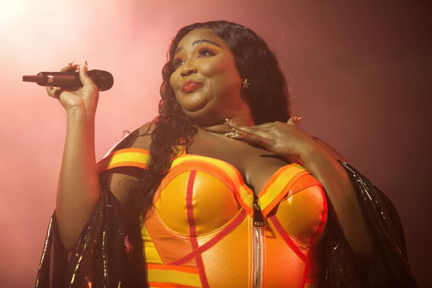 Lizzo wearing an orange bodysuit and holding a microphone