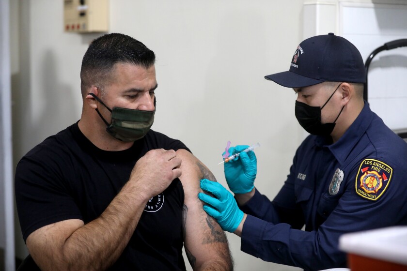 An L.A. Fire Department captain is given a Moderna COVID-19 vaccination from firefighter paramedic on Dec. 28 in Los Angeles.