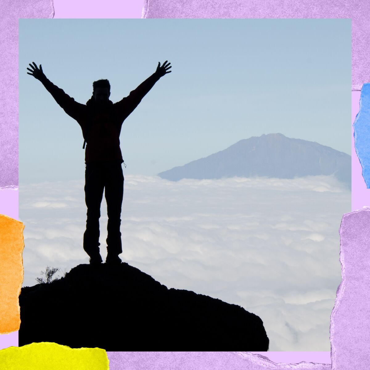 A man stands on top of a mountain, arms outstretched above his head, overlooking a bank of clouds.