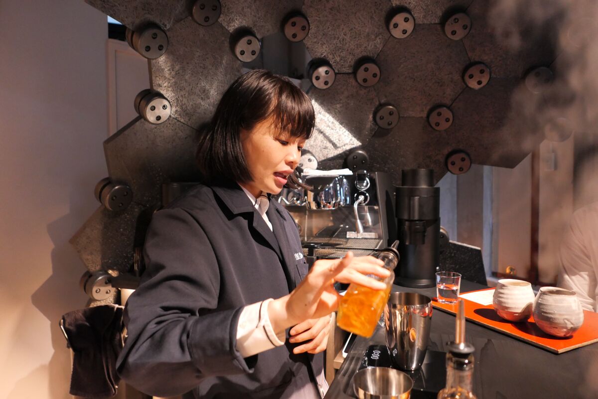 Cokuun barista Miki Suzuki stands in front of coffee-making machinery, pouring orange syrup into a drink.