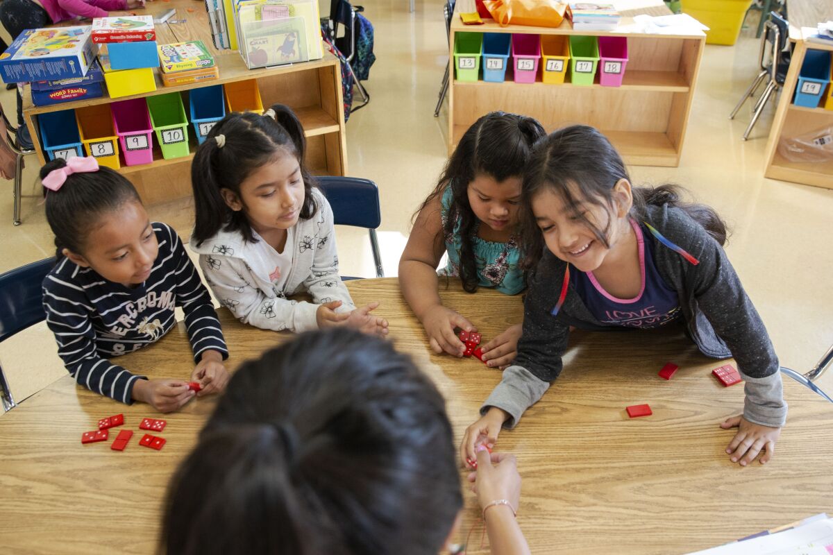 First graders play a math game with their teacher at a kid-size table in a classroom