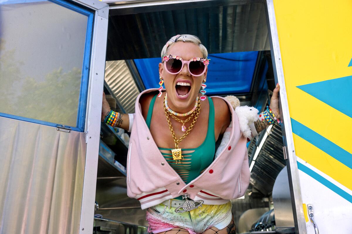  A female pop star wearing sunglasses leans out through an open door