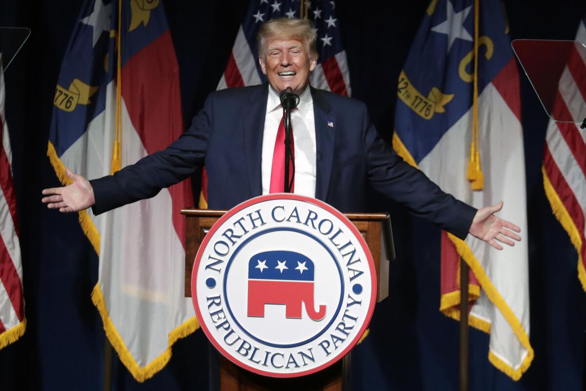 Former President Trump flings out his arms as he speaks at a lectern with the North Carolina Republican Party logo