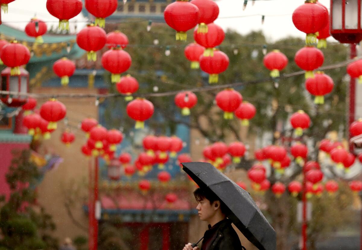 A person walks beneath an umbrella; above him are strings of red paper lanterns.