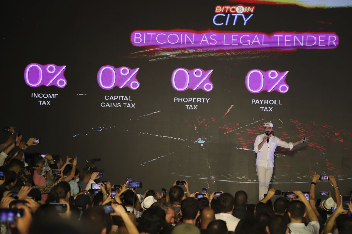 El Salvador's President Nayib Bukele is seen on stage, surrounded by different financial metrics in neon.