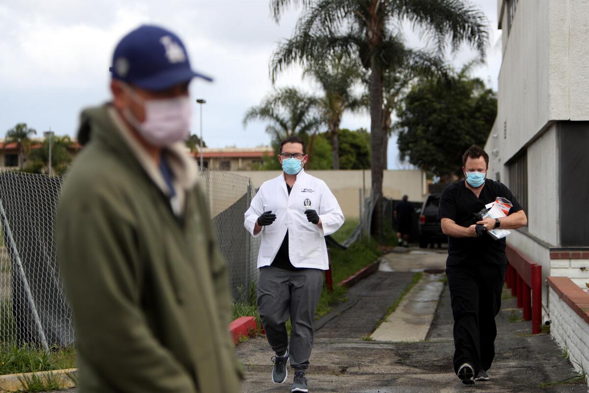 Dr. Matthew Abinante, center, and his office manager, Daniel Zike, walk toward Marcos Padilla to administer a test for the novel coronavirus in Huntington Beach on March 19.