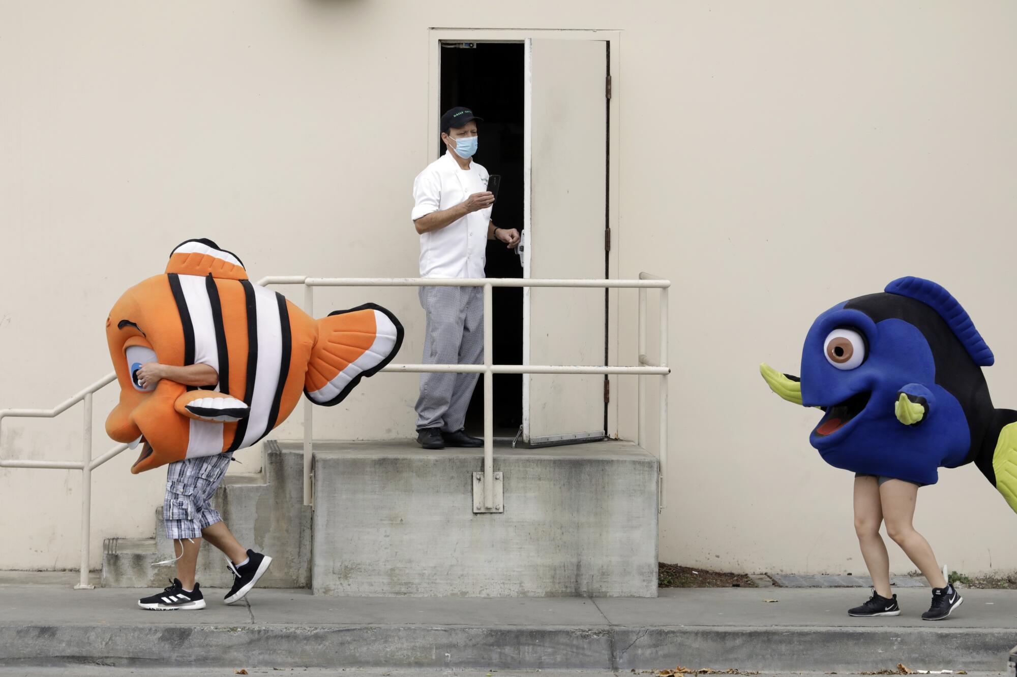 A couple of characters from the LAX Aquarium and an employee at the Westin Los Angeles Airport watch a car caravan protest on Century Boulevard. The protesters were demanding healthcare coverage during the coronavirus pandemic.