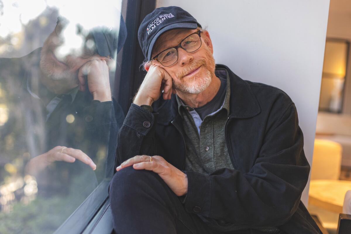 Ron Howard sits next to a window, wearing his trademark ball cap, and poses for a portrait.