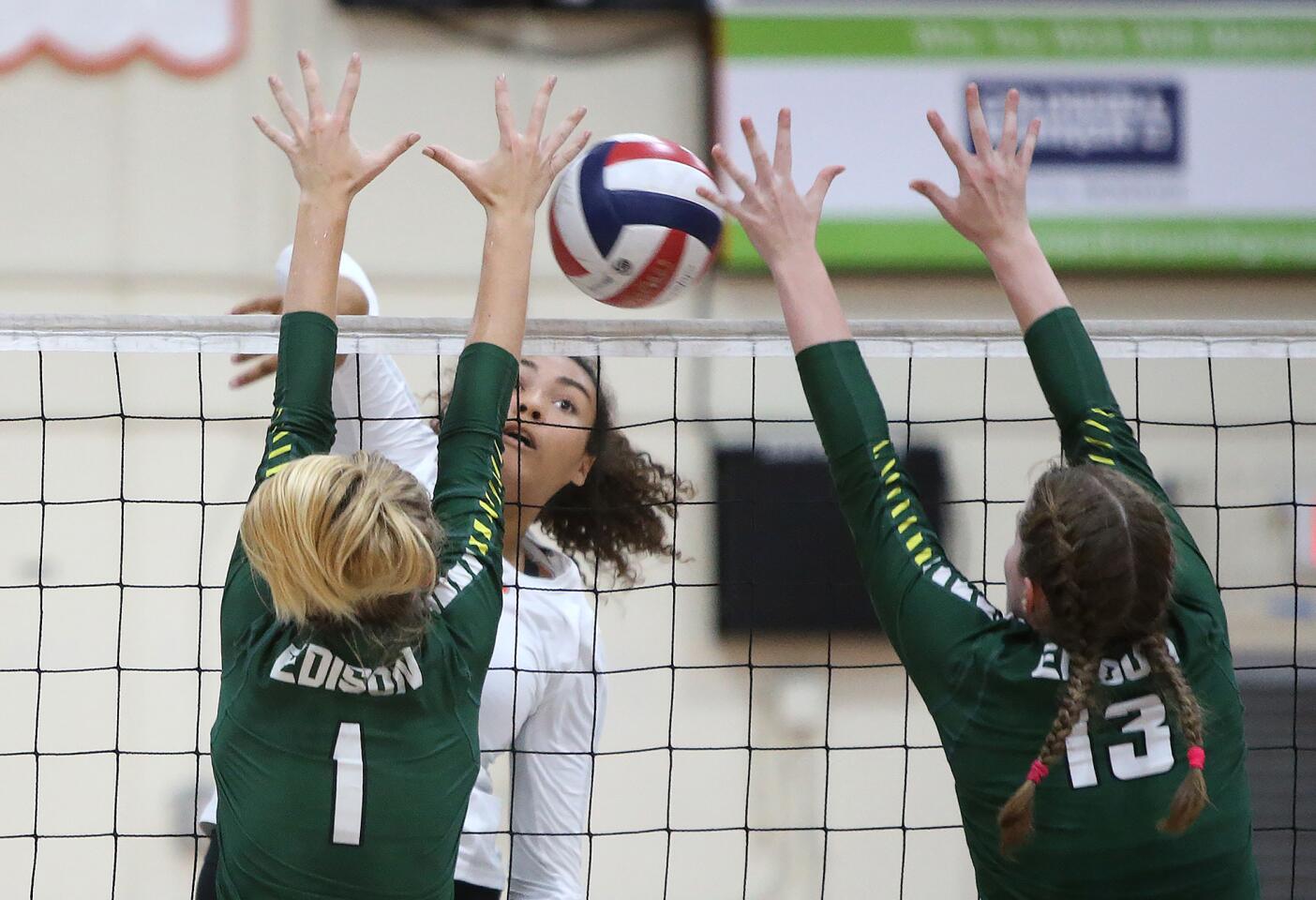 Huntington Beach High's Olivia Carlton puts the ball past Edison blockers Mia Christensen (1) and Taylor Torch (13) in girls volleyball on Tuesday at Huntington High.