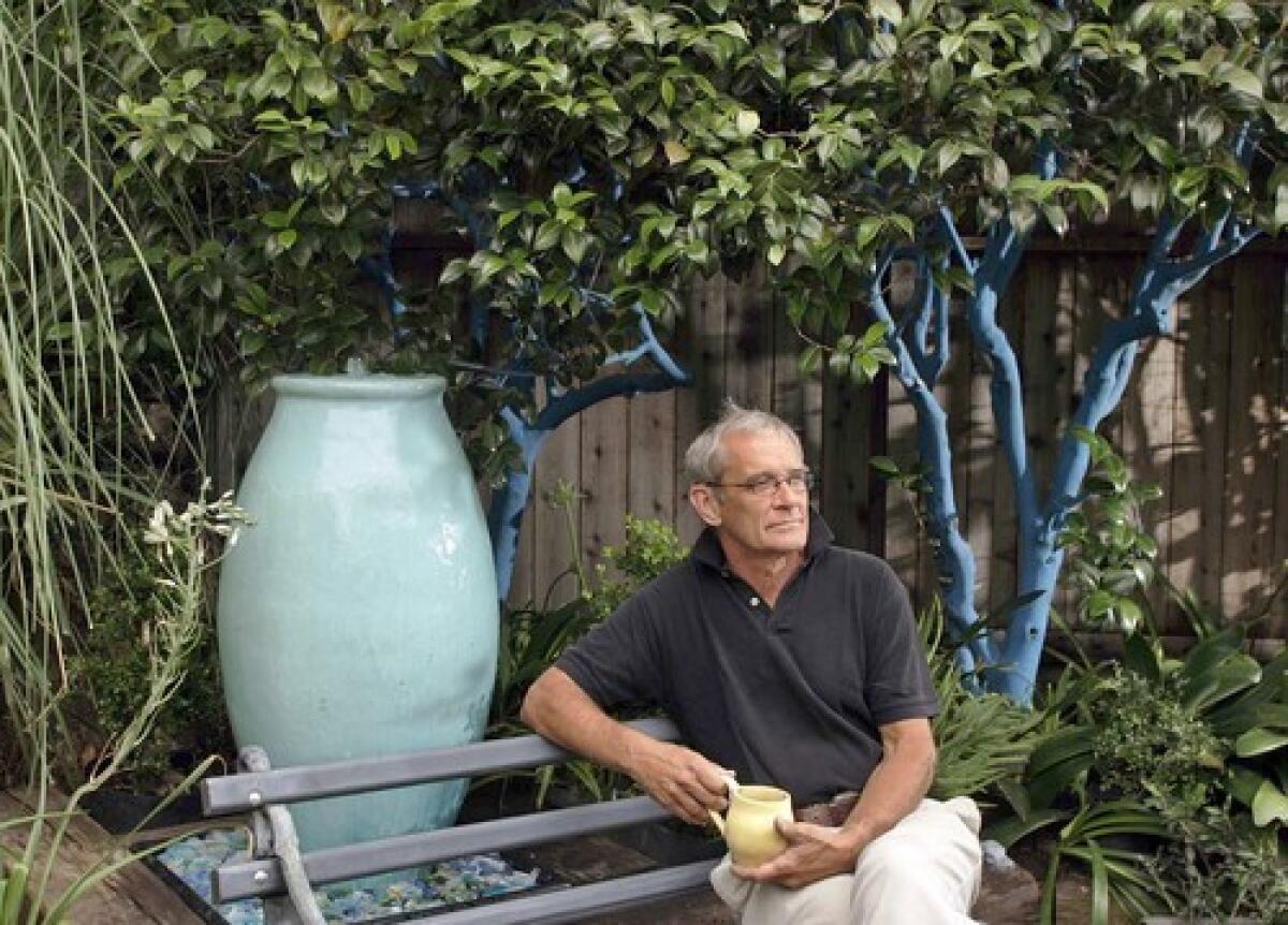 Landscape designer Ted Weiant in his backyard where he has tinted the trunks and branches of trees with latex paint, like this camelia that is painted blue.