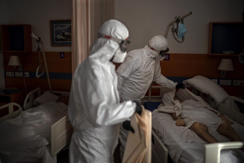 Separated by a curtain, a person sleeps in a bed as mortuary workers prepare the body of an elderly person who died of COVID-19 before removing it from a nursing home in Barcelona, Spain, Thursday, Nov. 19, 2020. Virus cases among the elderly are again on the rise across Europe, causing havoc and rising death tolls in nursing homes despite the lessons of a tragic spring. Authorities are in a race to save lives as they wait for crucial announcements on mass vaccinations. (AP Photo/Emilio Morenatti)