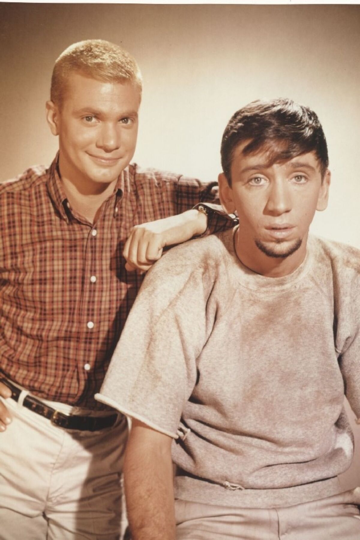 A sepia image of a young man resting his arm on another young man's shoulder.