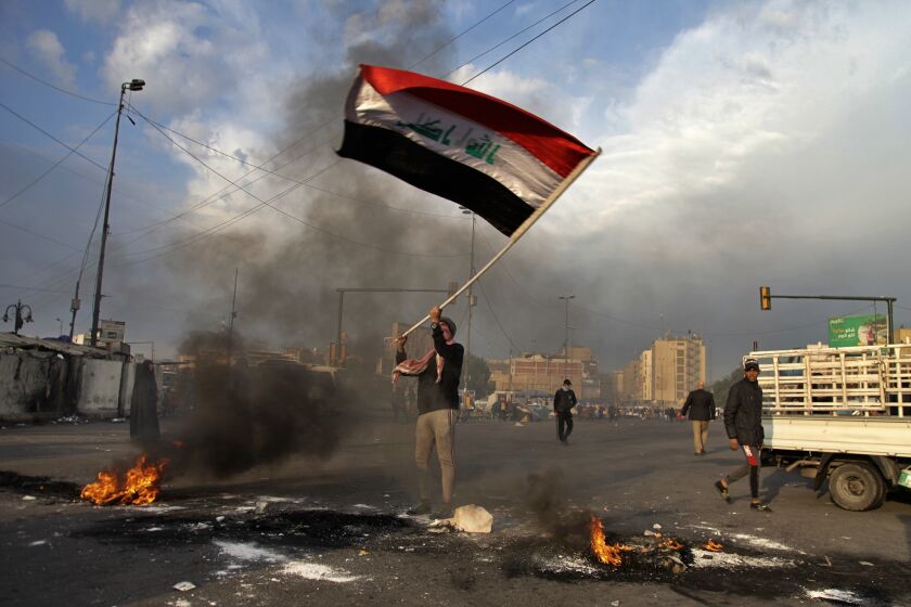 A protester waves the national flag while demonstrators set fire to close streets near Tahrir Square during a demonstration against the Iranian missile strike in Baghdad, Iraq, Wednesday, Jan. 8, 2020. Iran struck back at the United States early Wednesday for killing a top Revolutionary Guard commander, firing a series of ballistic missiles at two military bases in Iraq that house American troops in a major escalation between the two longtime foes. (AP Photo/Khalid Mohammed)