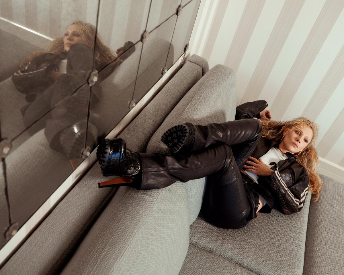 Juno Temple lies on a couch with her feet up against the mirror behind it