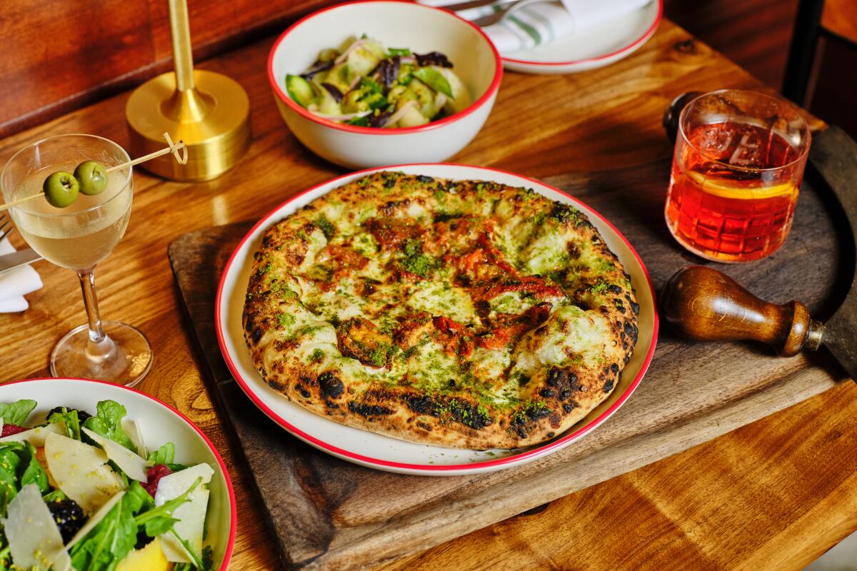 A pizza with a cocktail and other dishes on a wooden table