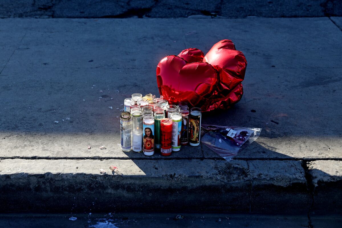 Candles and red heart balloons on a sidewalk.