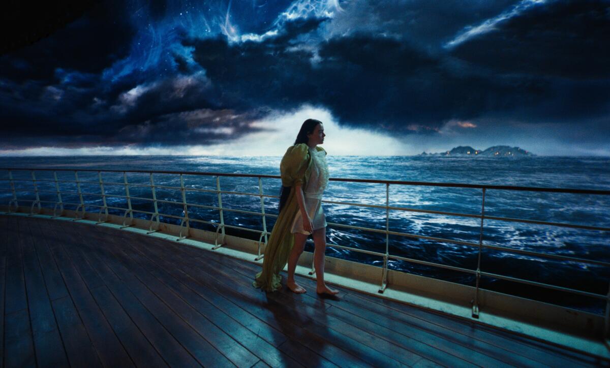 A woman strolls the deck of a ship under moody dark skies in "Poor Things."