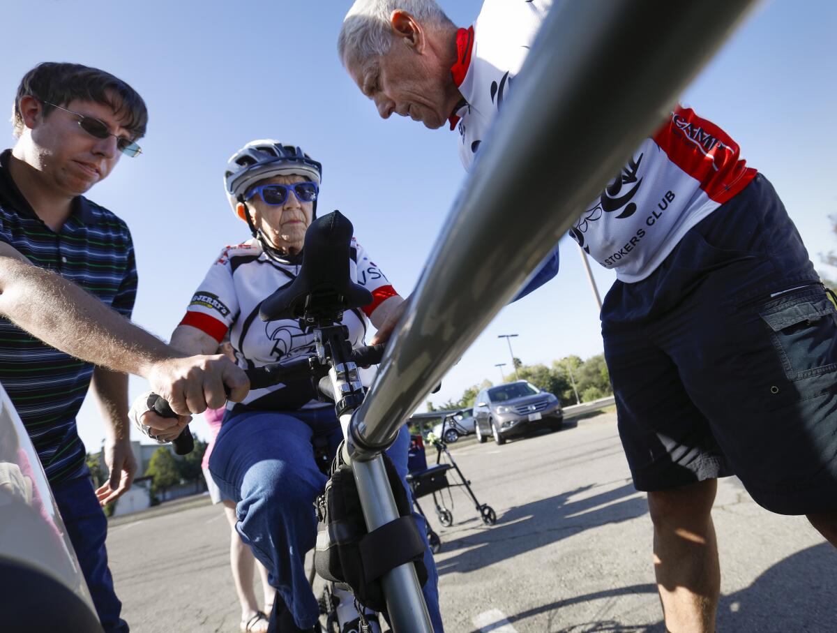 June Clark, 86, center, a resident of Cypress Court, a senior living community in Escondido, gets on a bicycle for the first time ever, assisted by her grandson, Thomas Clark, left, and Dave White, right, founder and president of the Blind Stokers Club, who rode with her on a tandem bike at Kit Carson Park in Escondido on Sept. 19.