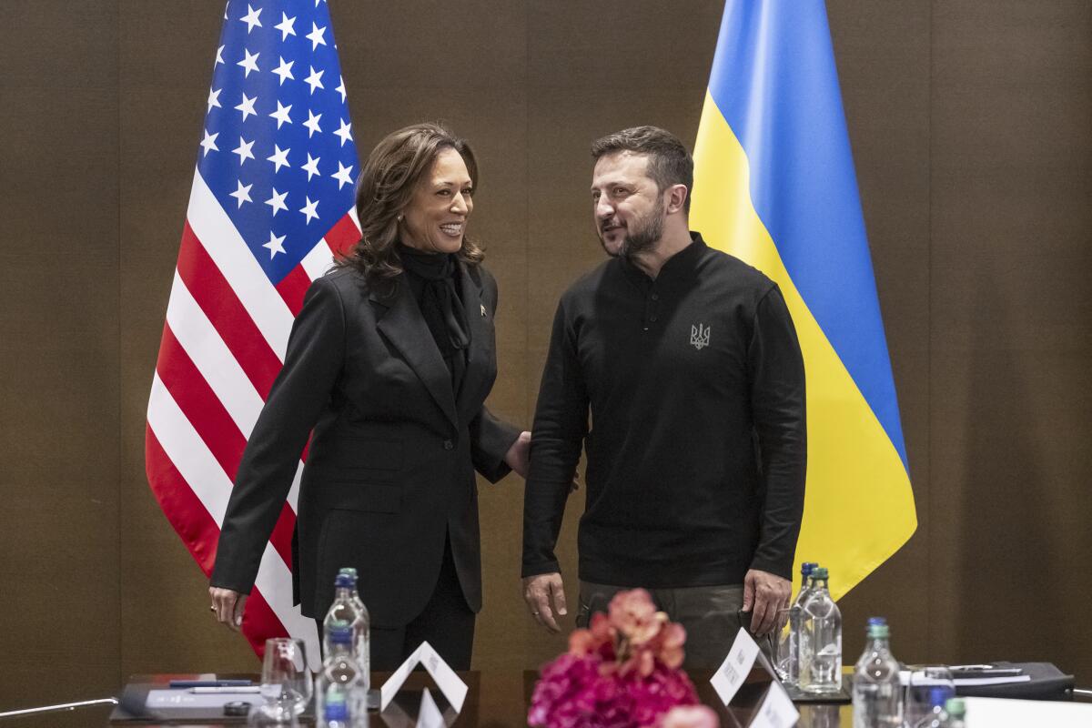 Vice President Kamala Harris touches the arm of Ukrainian President Volodymyr Zelensky near American and Ukrainian flags.