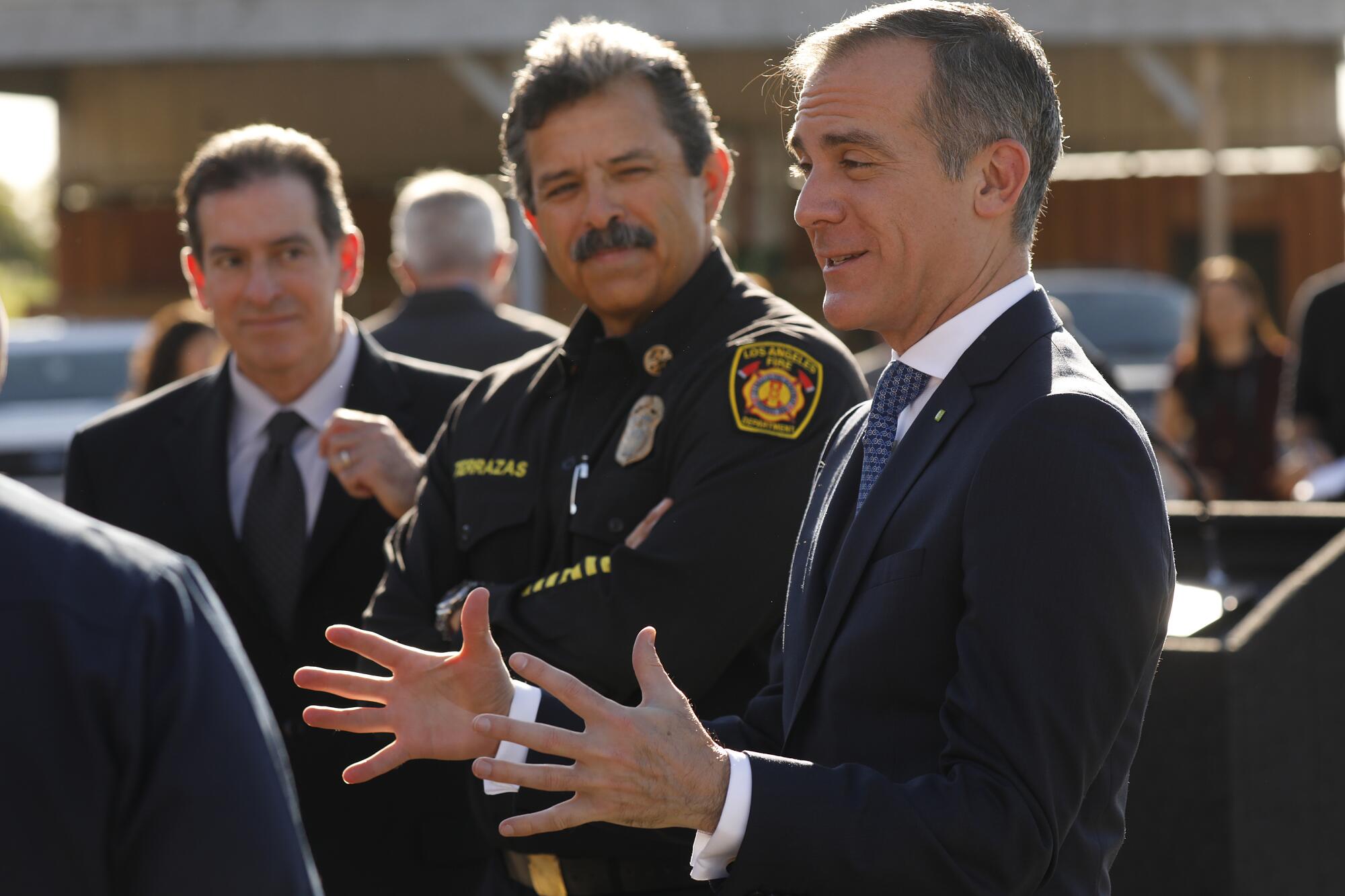 A fire chief in uniform stands between men in suits at a news conference.