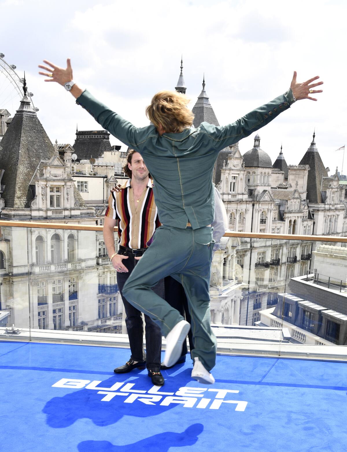 A rear view of a man in a green suit jumping in the air with arms and legs spread