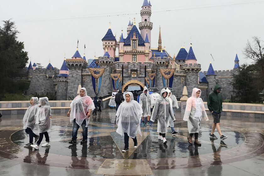 A group of people in rain ponchos walking in front of Sleeping Beauty Castle at Disneyland