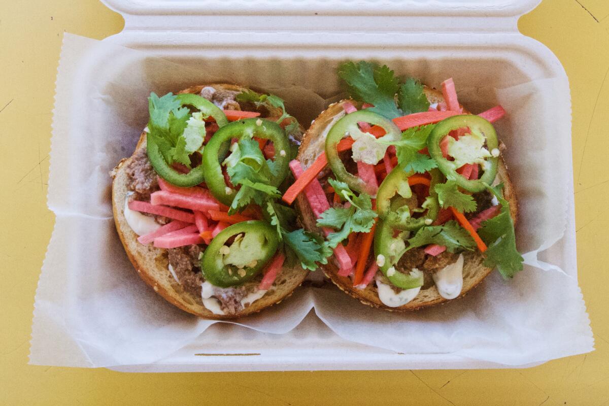 An overhead photo of an open-faced Kitchen Mouse bagel topped with walnut spread, jalapeos and pickled veg in a takeout box
