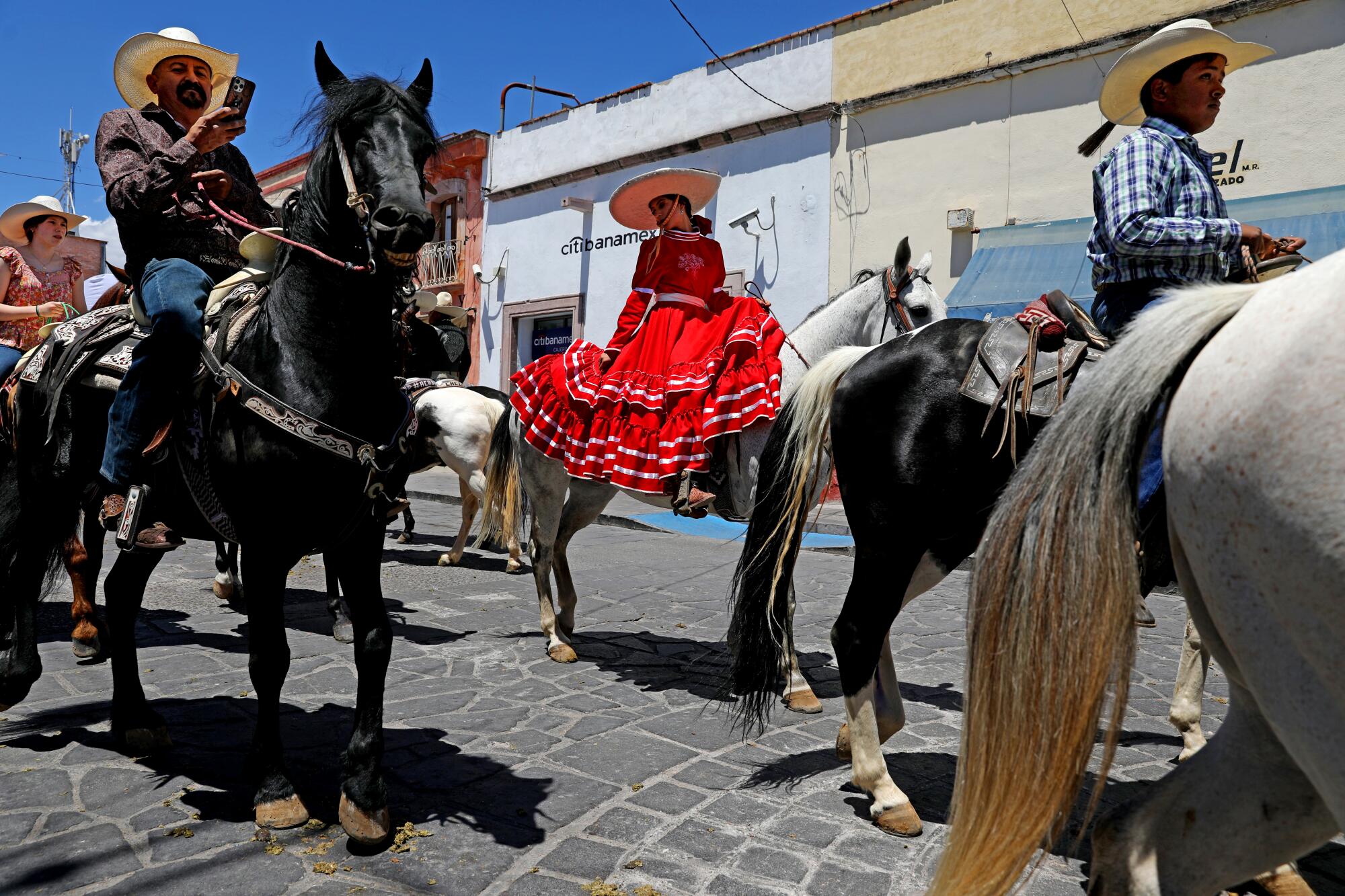 Charros participate in a traditional parade of horses on a cobbled Mexican street. 
